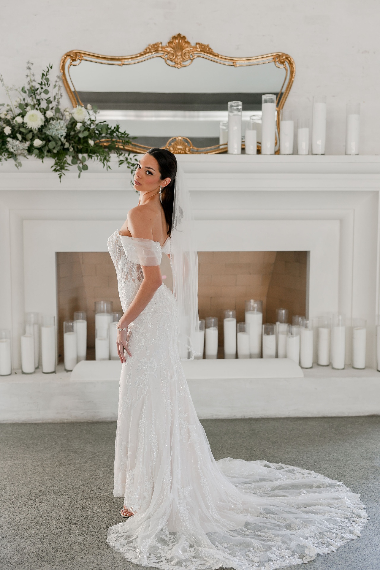 Real bride — bridal glam and sleek ponytail with cathedral veil beside a candlelit fireplace